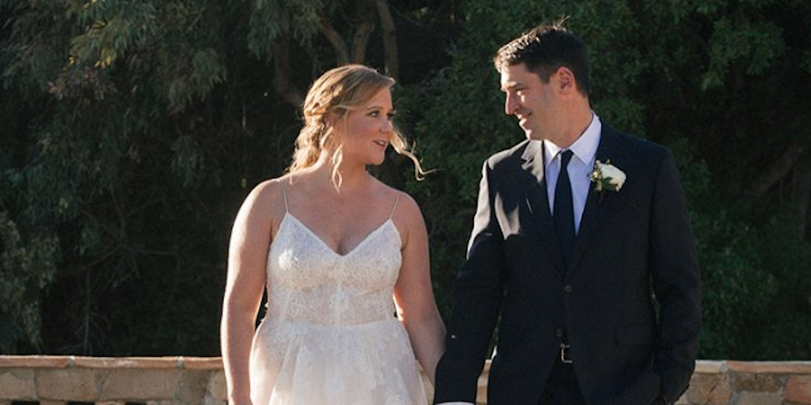 Amy Schumer and her new husband smile at each other while holding hands