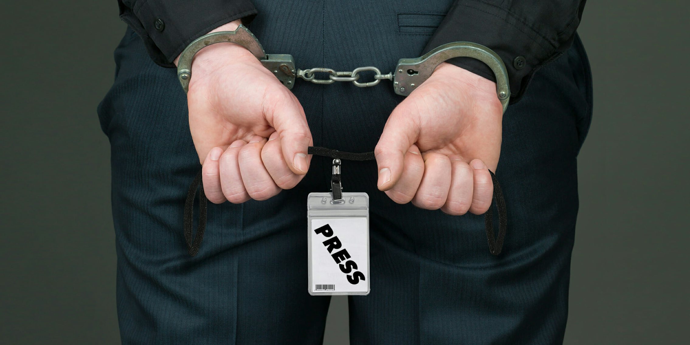 Handcuffed journalist holding press credentials