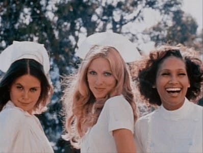 Three nurses stand smiling in uniform in a scene from night call nurse