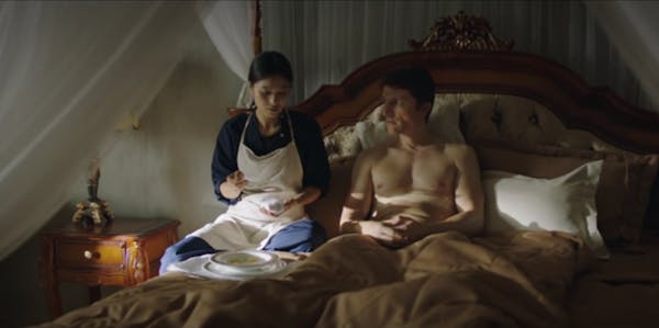 A scene from the housemaid showing a woman in an apron sitting on a bed next to a topless man
