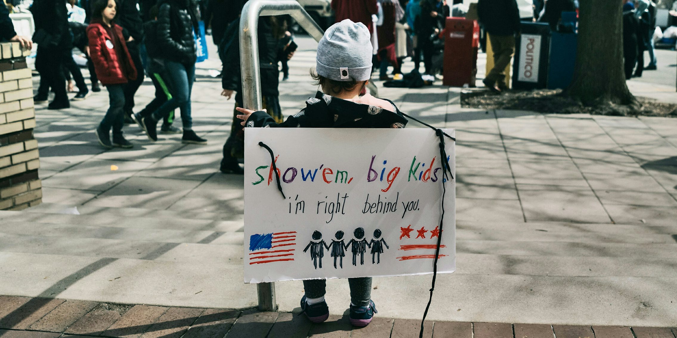 Child with 'show 'em big kids, i'm right behind you' sign at March For Our Lives