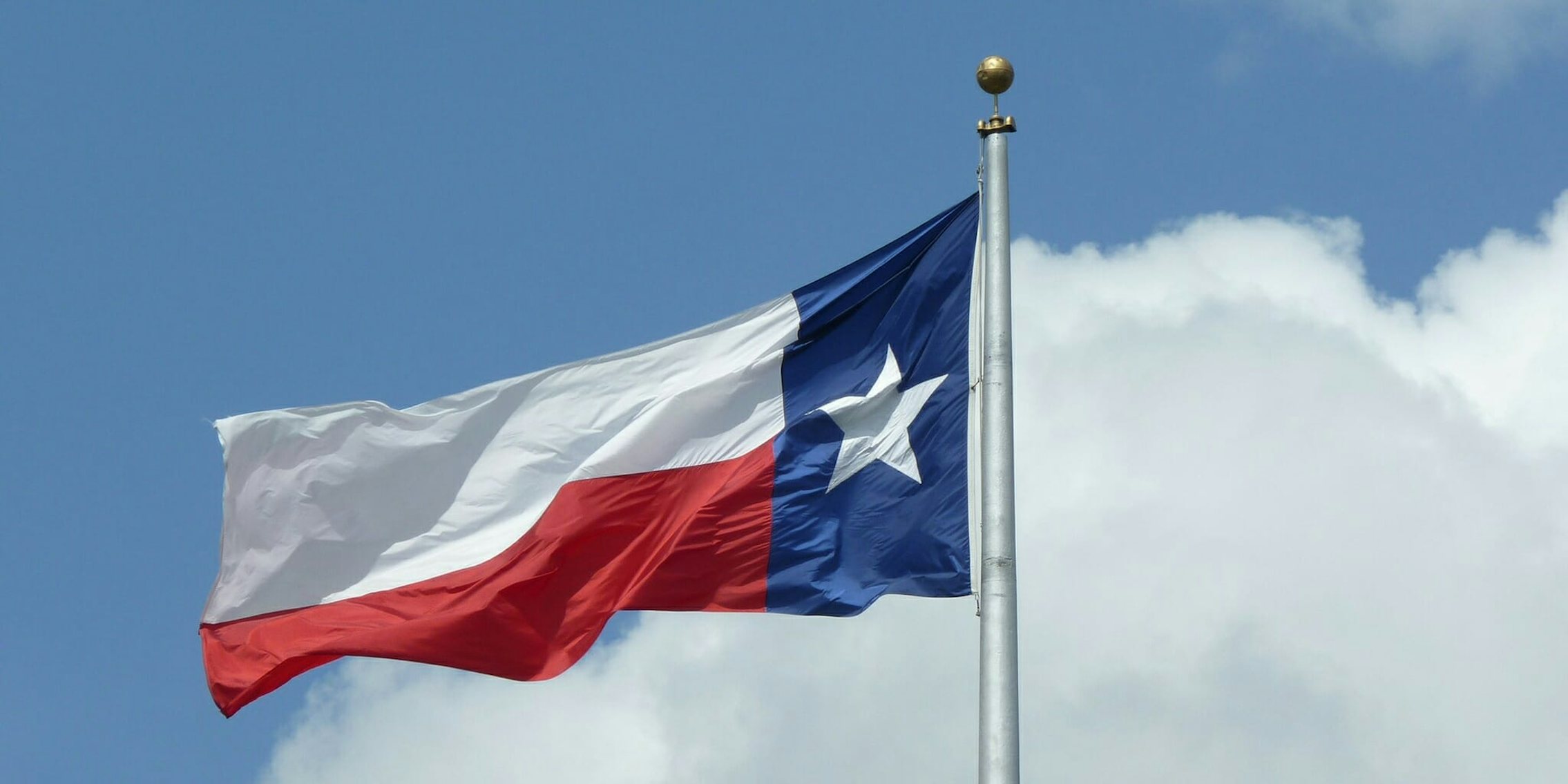 The Texas flag on a pole in a cloudy sky.