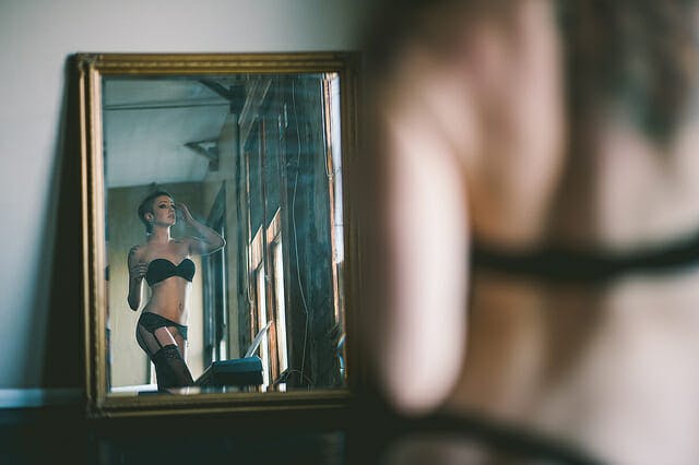 A queer model stares at themselves in the mirror in this image.