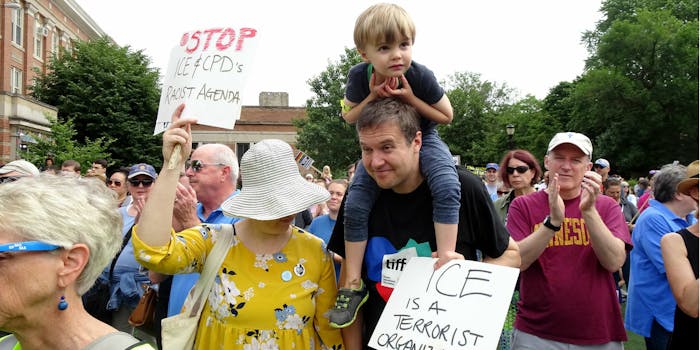 A family at an ICE protest in Chicago with signs that say 'STOP ICE and CBP's Racist Agenda' and 'ICE is a terrorist organization.'