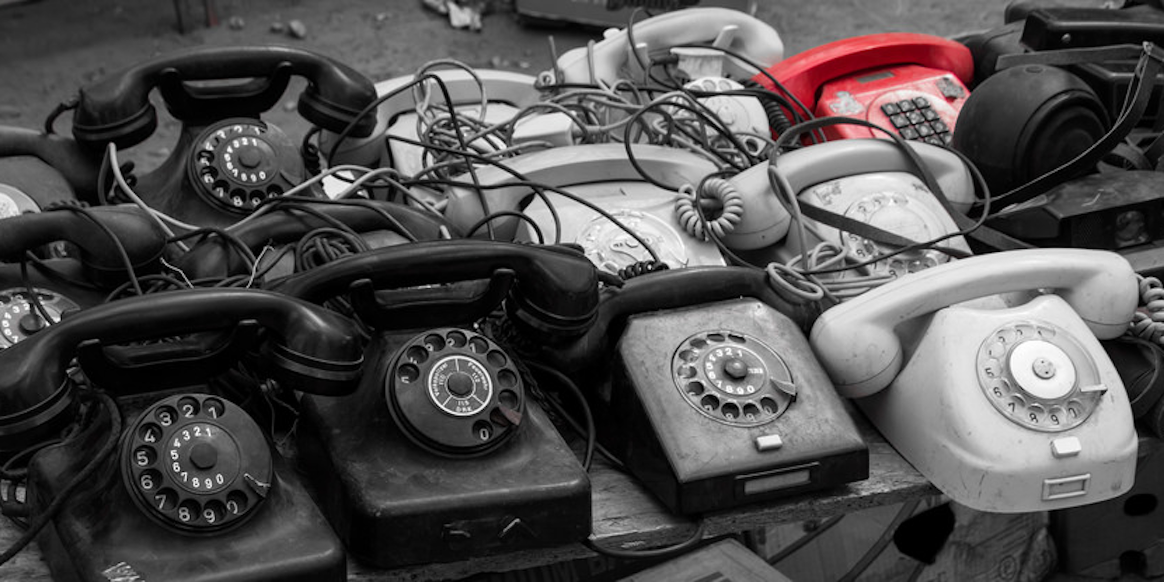 A pile of rotary phones in black and white, one red
