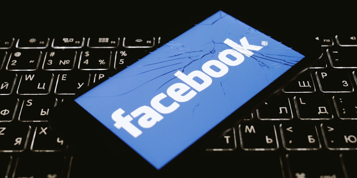 facebook logo on broken phone, sitting on top of cyrillic keyboard