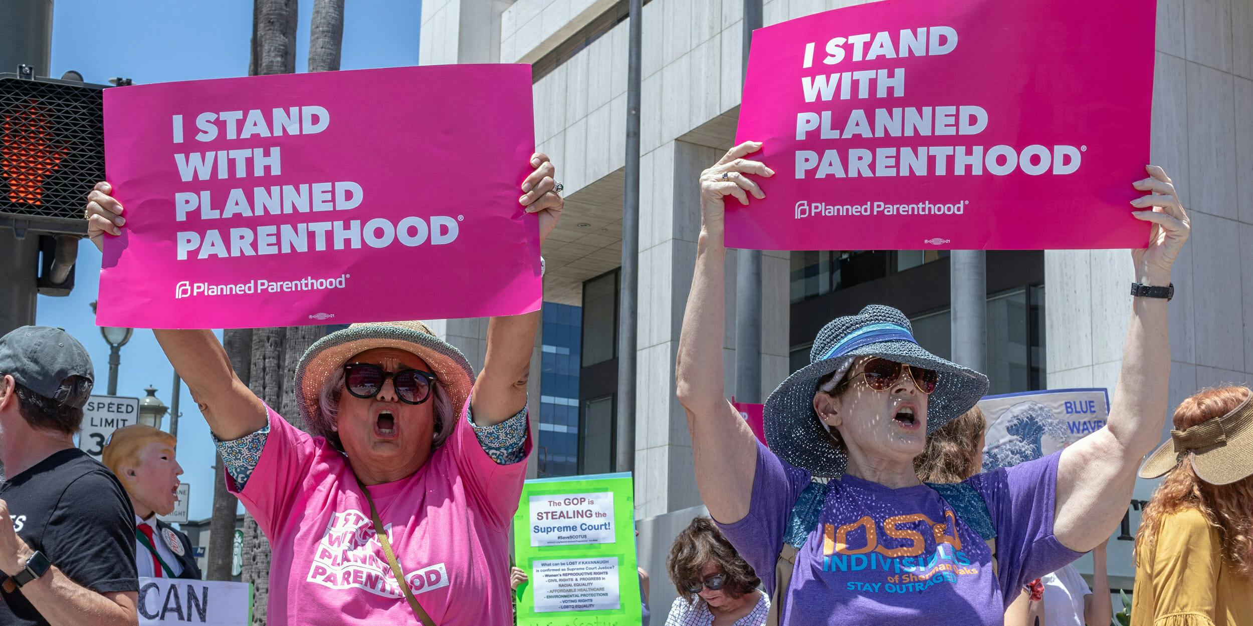 women hold "i stand with planned parenthood" signs at protest