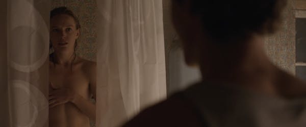 A woman stands naked in the shower as a man looks on in a scene from obsession