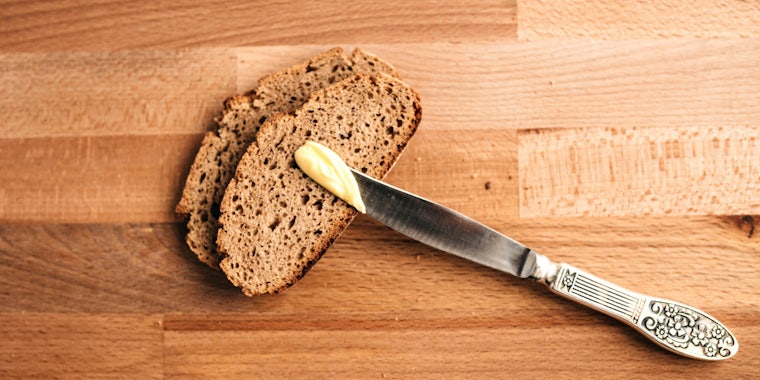 A knife with butter rests on two slices of bread