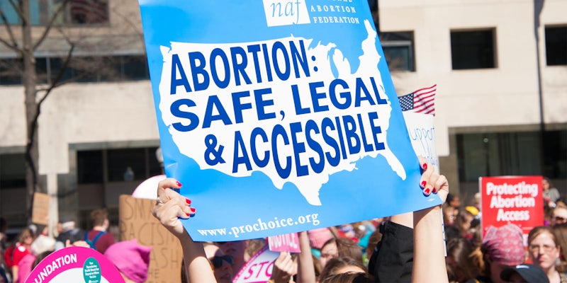 woman holding 'abortion: safe, legal & accessible' protest sign
