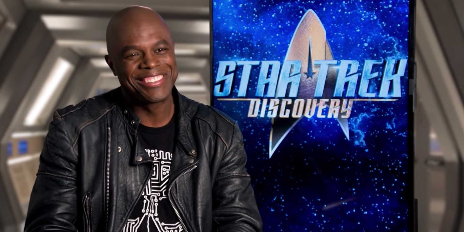 Star Trek Discover actor Chris Obi smiles during an interview in front of a Star Trek banner