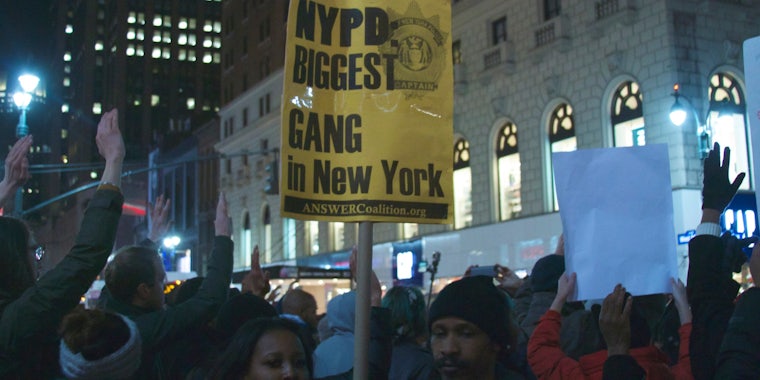 A yellow sign reads 'NYP Biggest Gang in New York' at a protest for Eric Garner