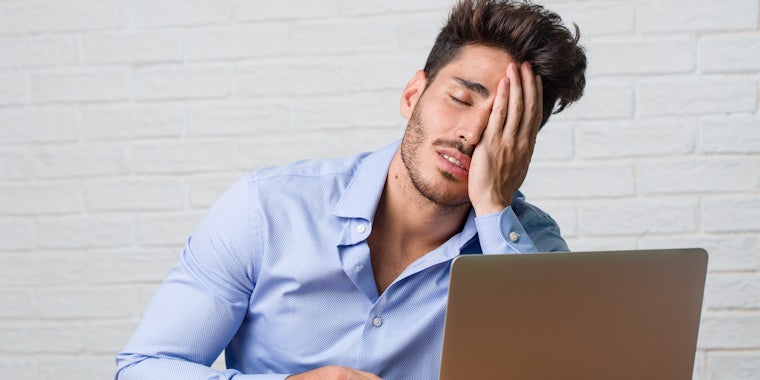 exasperated man with hand on face in front of laptop