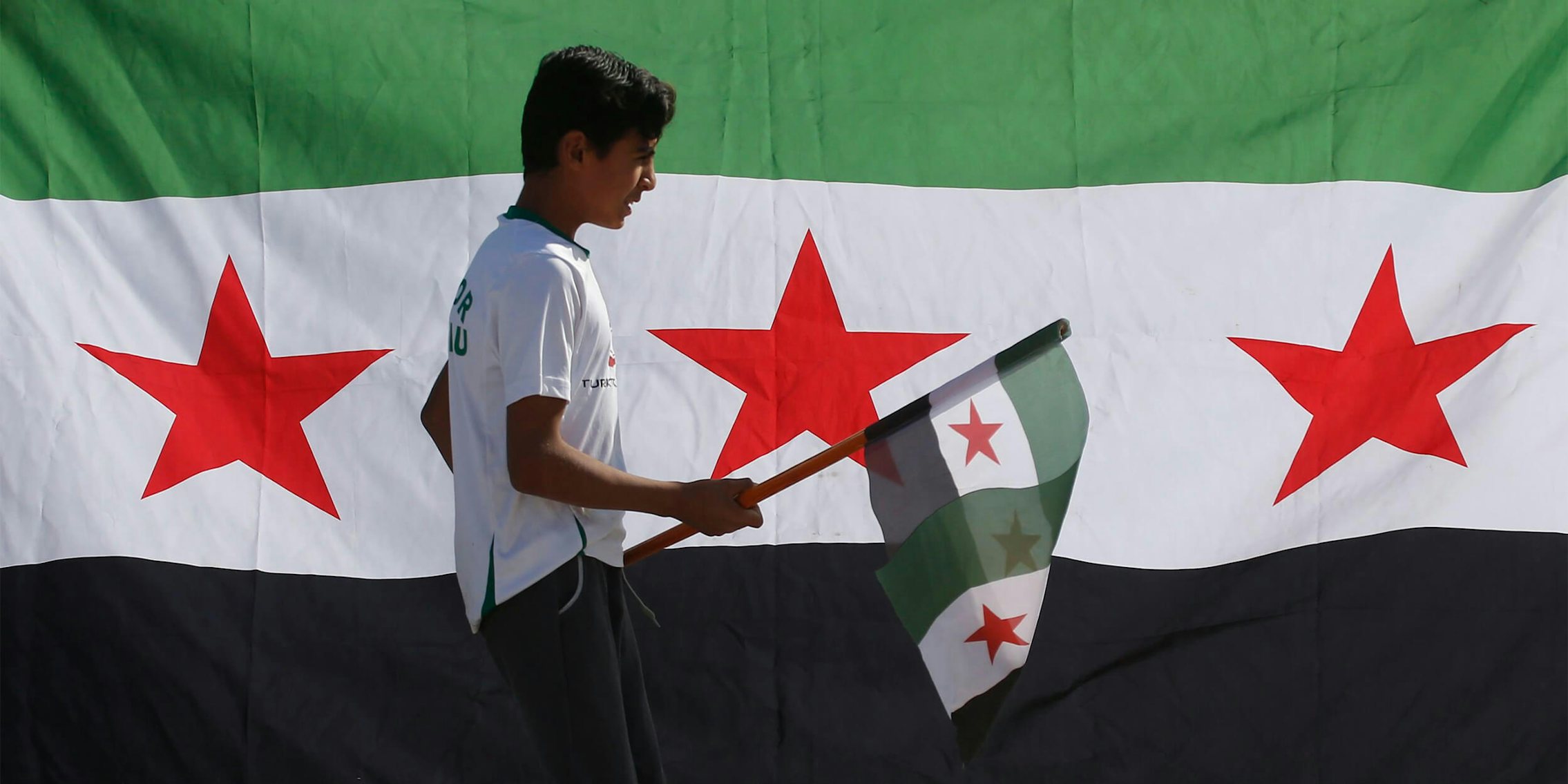 Syrian youth holds revolutionary flag in front of Syrian flag