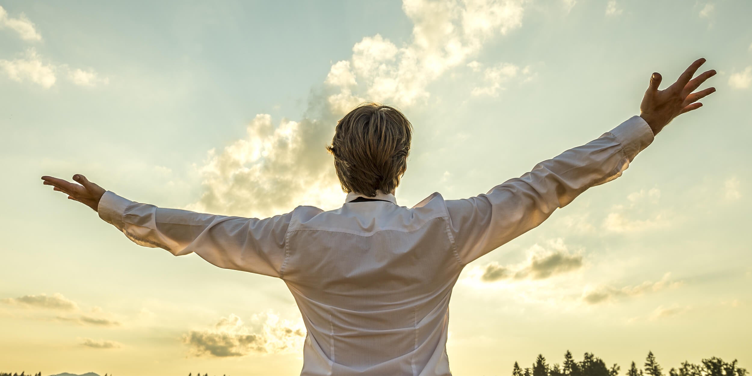 man in dress shirt raising his hands to the sky