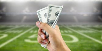 Person holding cash in front of football field