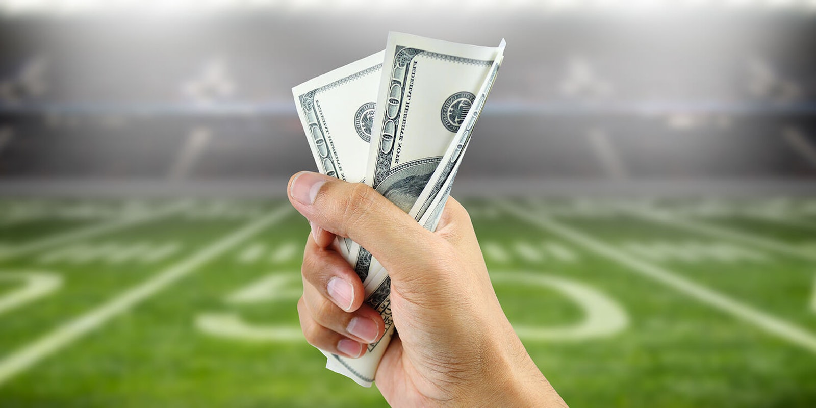 Person holding cash in front of football field