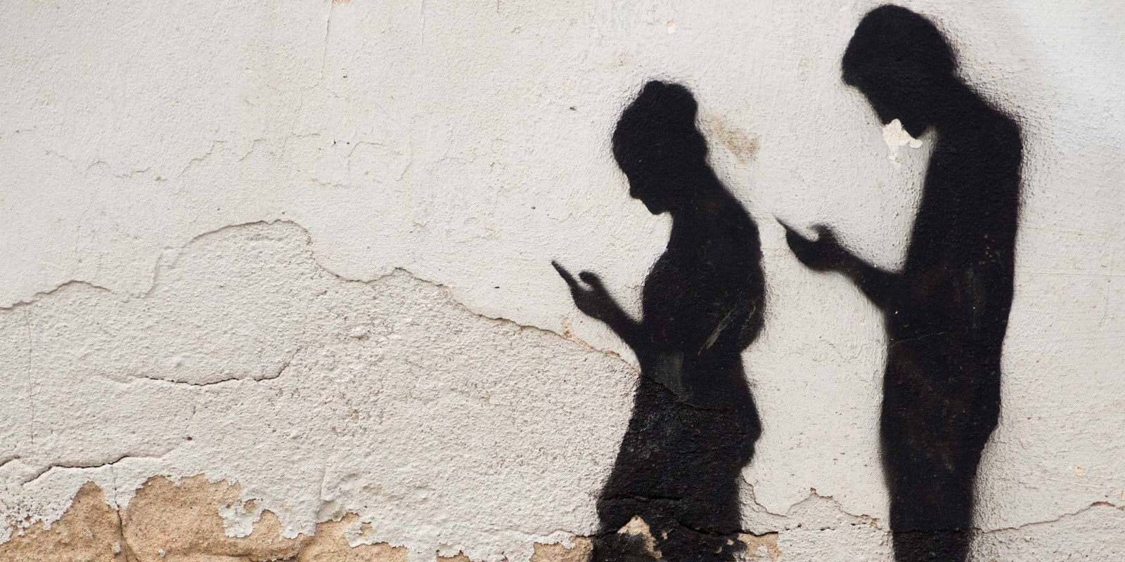 Shadows of people looking at their phone against a wall