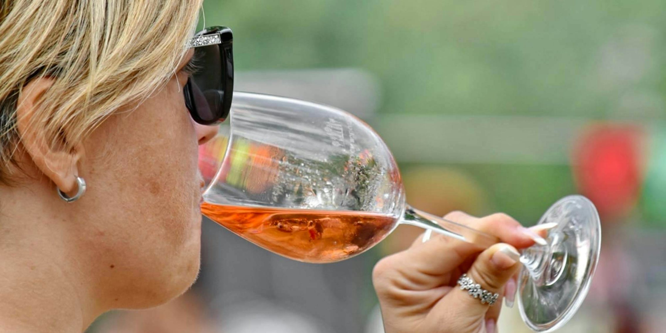 A woman with short blonde hair drinking from a wine glass
