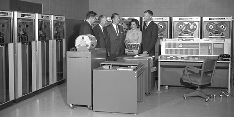 A group of people standing in front of computers from the 1960s