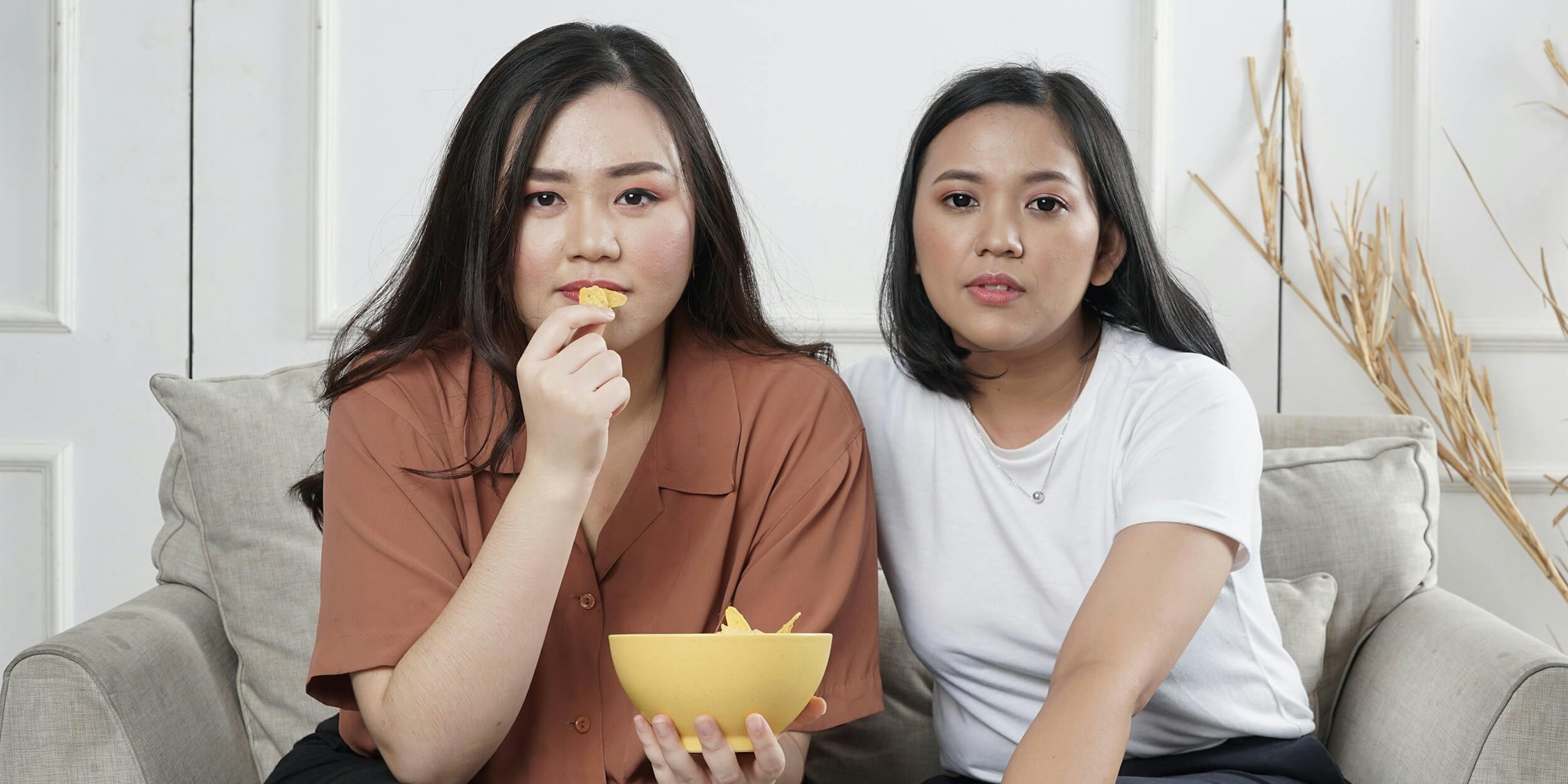 women sitting on couch eating chips
