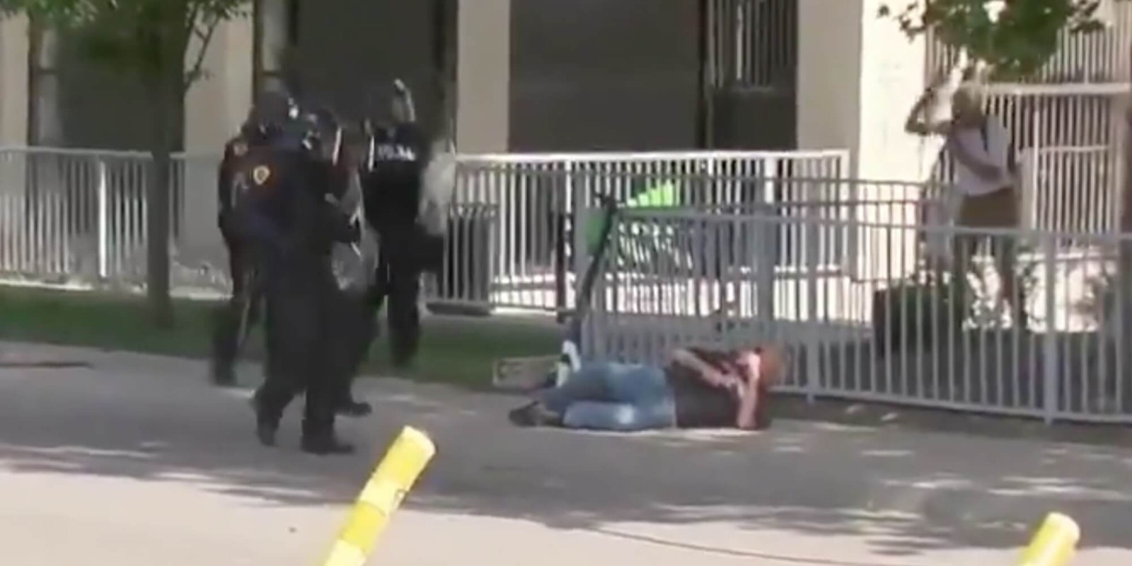 An old man laying on the pavement next to cops in riot gear