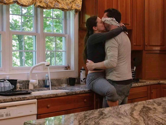 Couple kissing in a kitchen, the man has a blindfold on