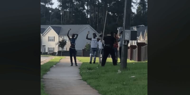 Screenshot of a video of six black teens with their hands in the air while a cop holds a gun on them