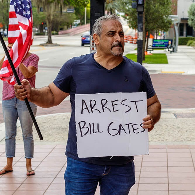 man waving a flag holding an "arrest bill gates" sign 5g conspiracies