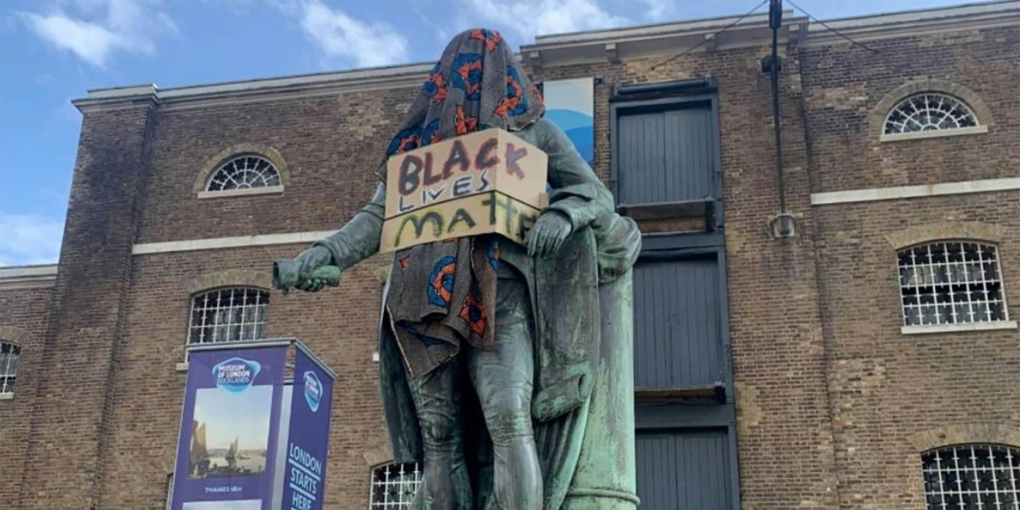 robert milligan statue covered with blanket and "Black Lives Matter" sign