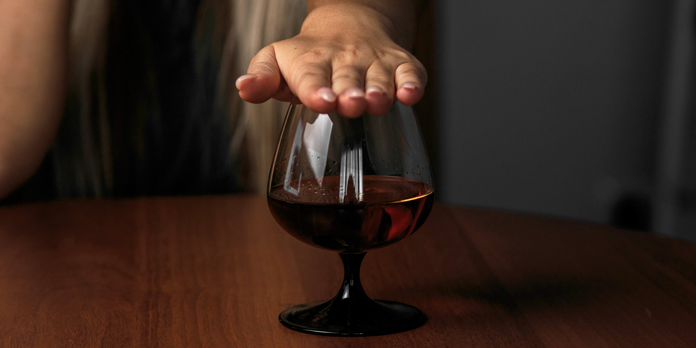 woman covering a glass of alcohol with her hand