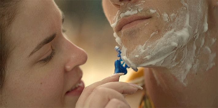 Woman shaving man's face with a razor.
