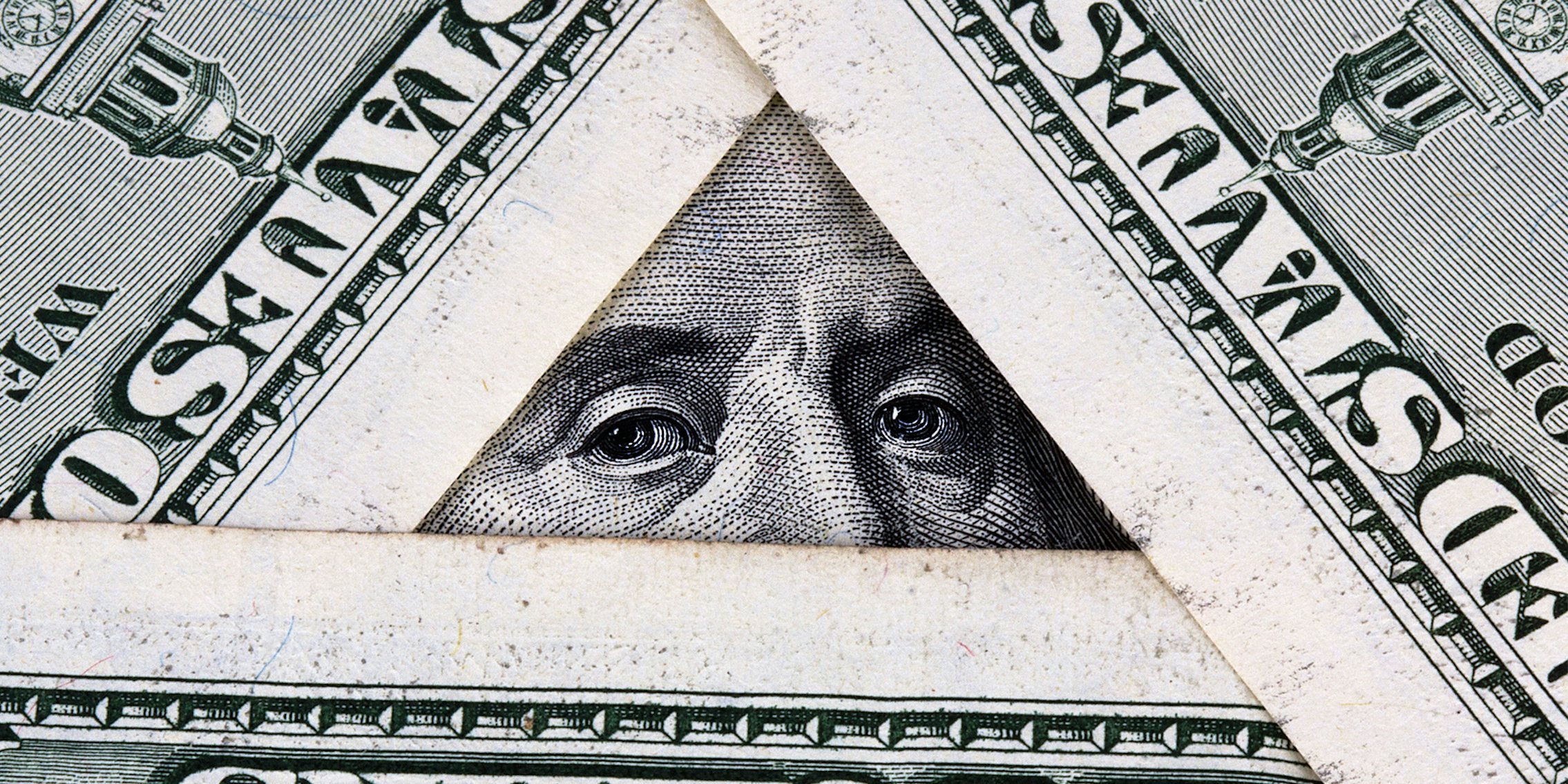 hundred dollar bills arranged in a triangle, showing benjamin franklin's eyes