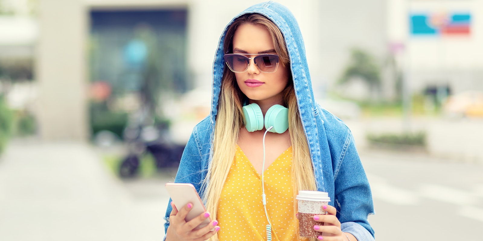 woman in hoody and sunglasses walking with coffee and phone
