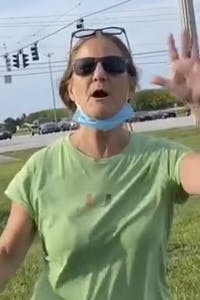 ranting woman in green miami shirt with sunglasses on face and glasses on head, mask around neck, hands raised
