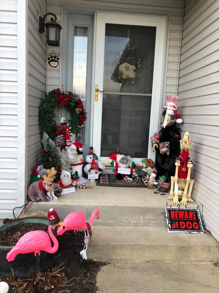 Two pink plastic flamingoes stand in front and to the left of the porch which contains all the decorations described previously. One flamingo wears a red bobble hat and the other one a red scarf.