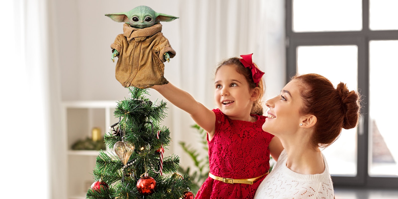 mother holding up little girl to place grogu on top of the christmas tree