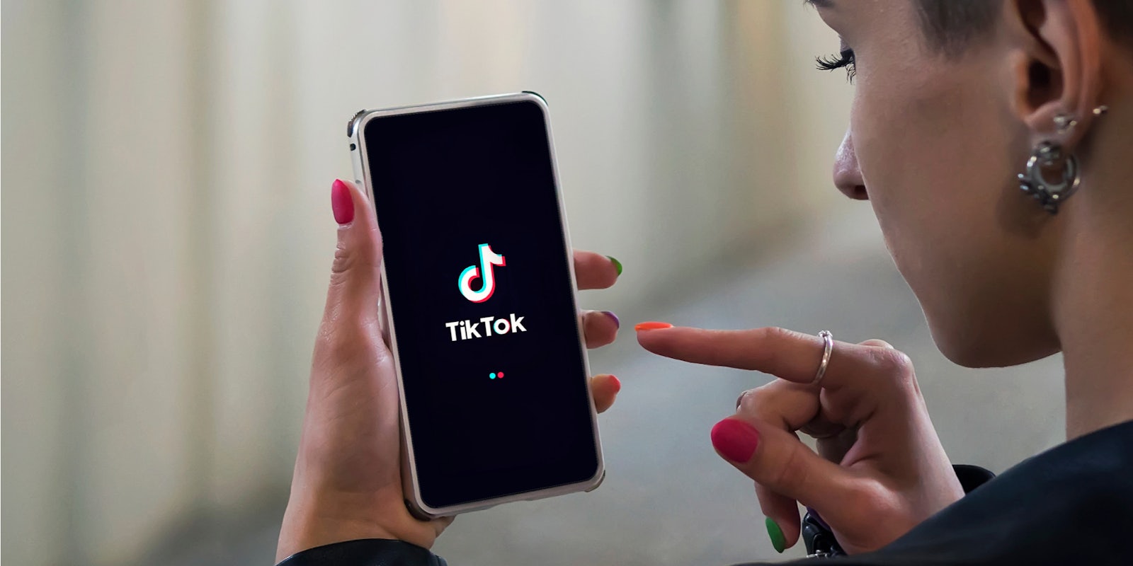 side profile of person with earrings and colorful nails using tiktok