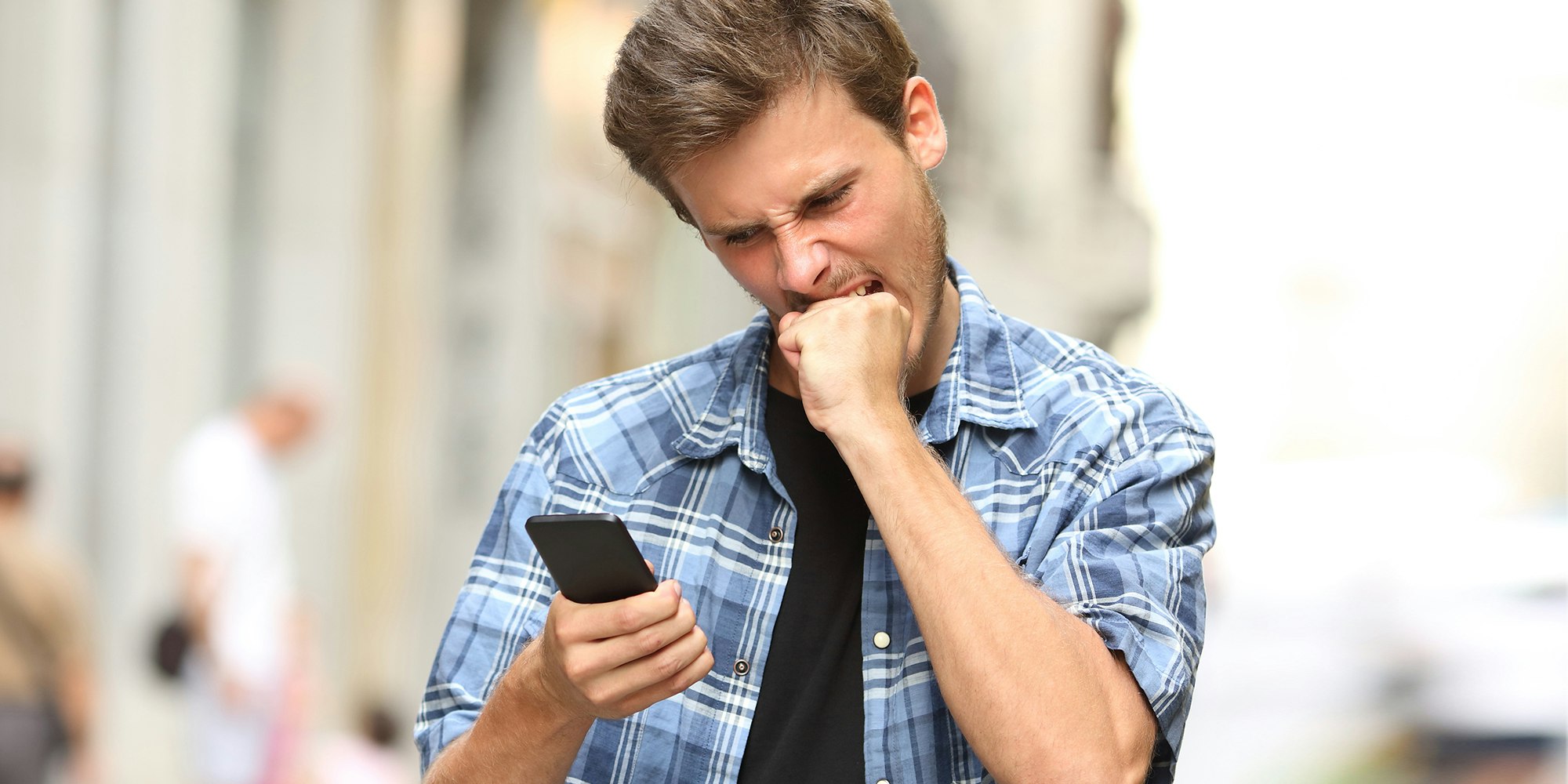 man biting fist while looking at phone
