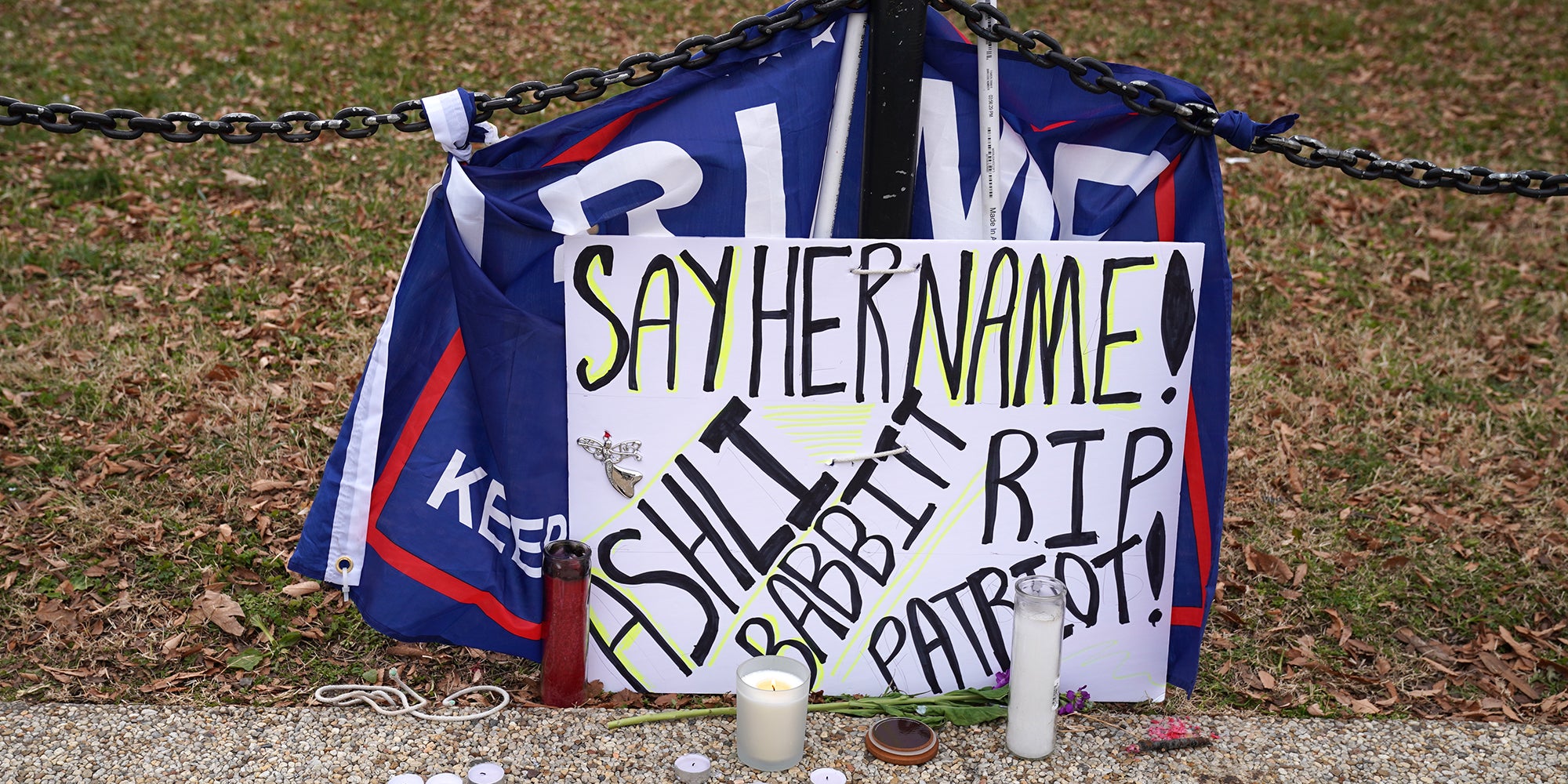 hand-written poster reading "Say her name! Ashli Babbitt RIP Patriot!" with Trump flag and candles