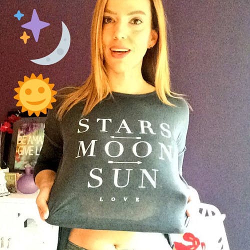 Picture of Danielle smiling with her shirt that's branded the same as her astrology services. The shirt reads 'Stars, moon, sun, and love'