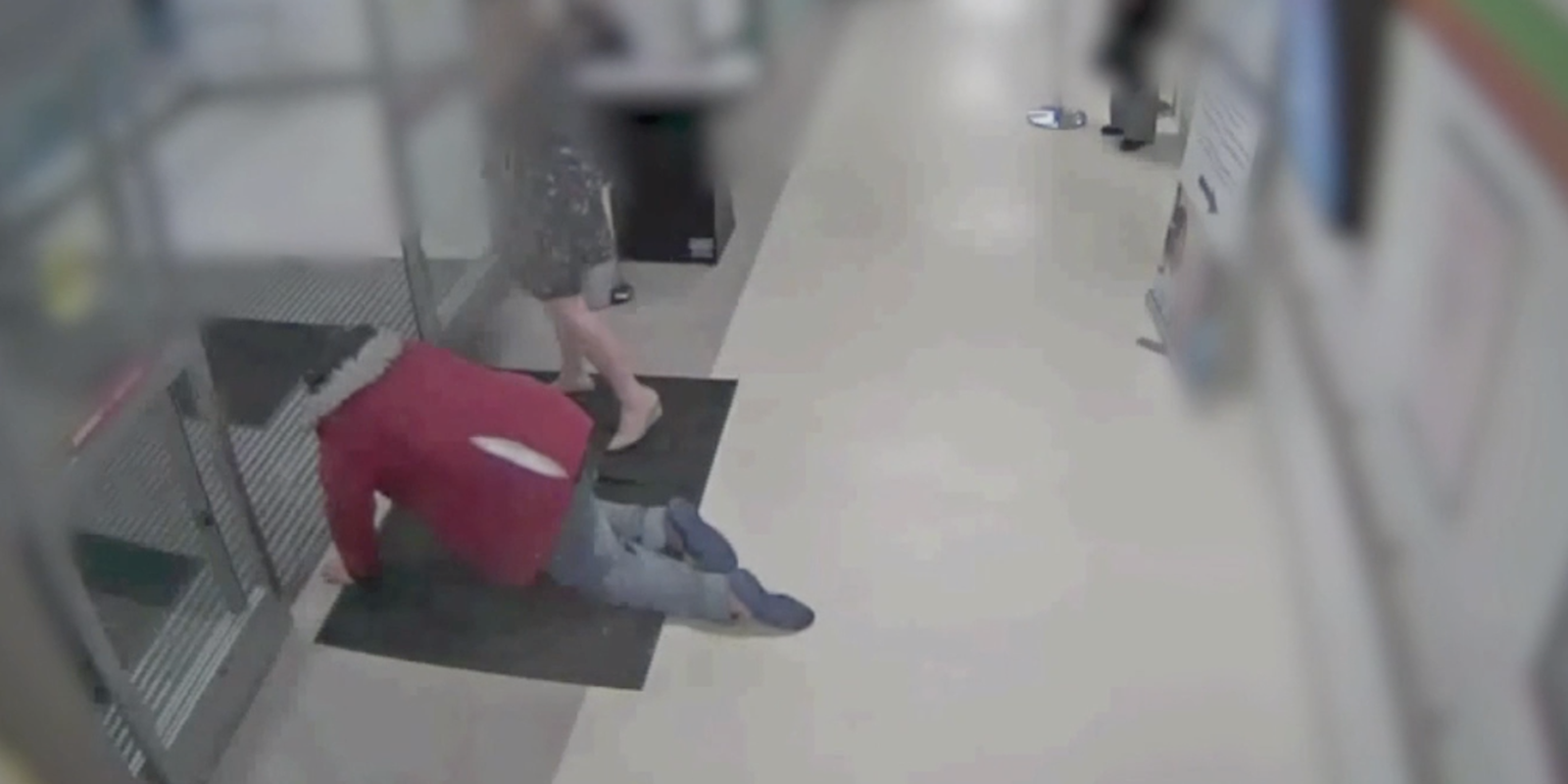 a man in a red shirt and jeans crawls into the hospitals exit beside a person in a black dress