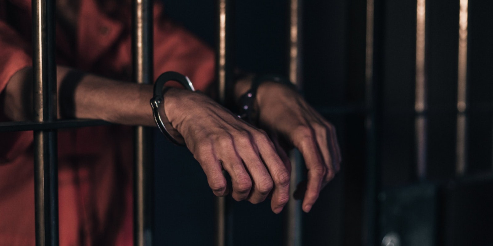 A person in handcuffs behind bars