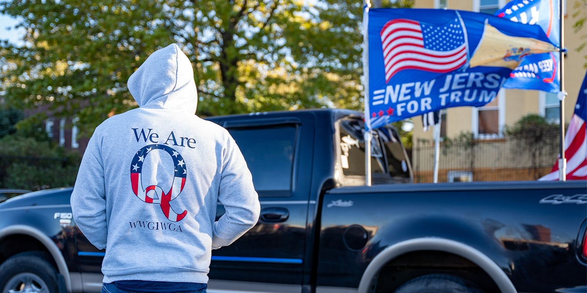person wearing 'We Are Q WWG1WGA' hooded sweatshirt in front of truck with New Jersy For Trump flag