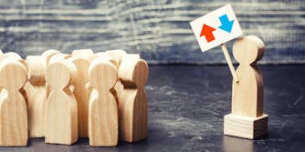 wooden figure on platform holding reddit upvote/downvote icon sign, in front of crowd of other wooden figures