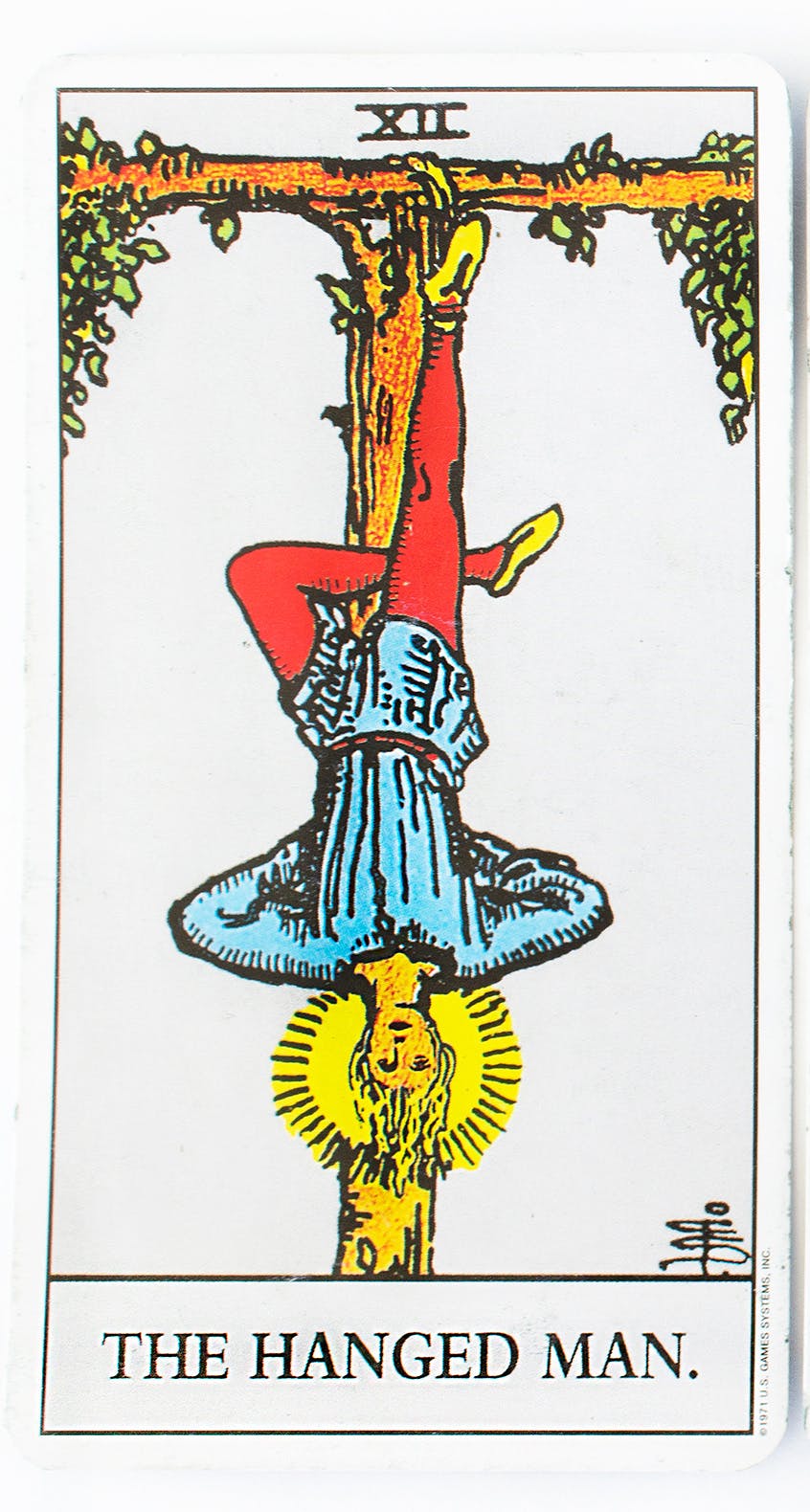 the hanged man from the Rider-Waite tarot deck. image of a man hanging by one ankle upside down on a cross.