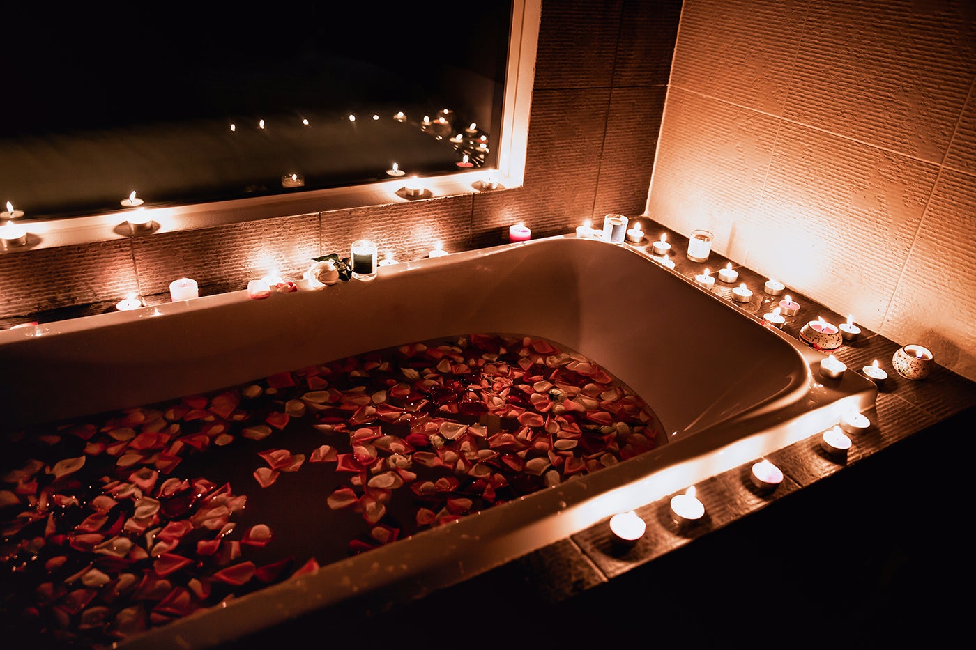 Bathtub lined with candles and flowers, rose petals float in the water