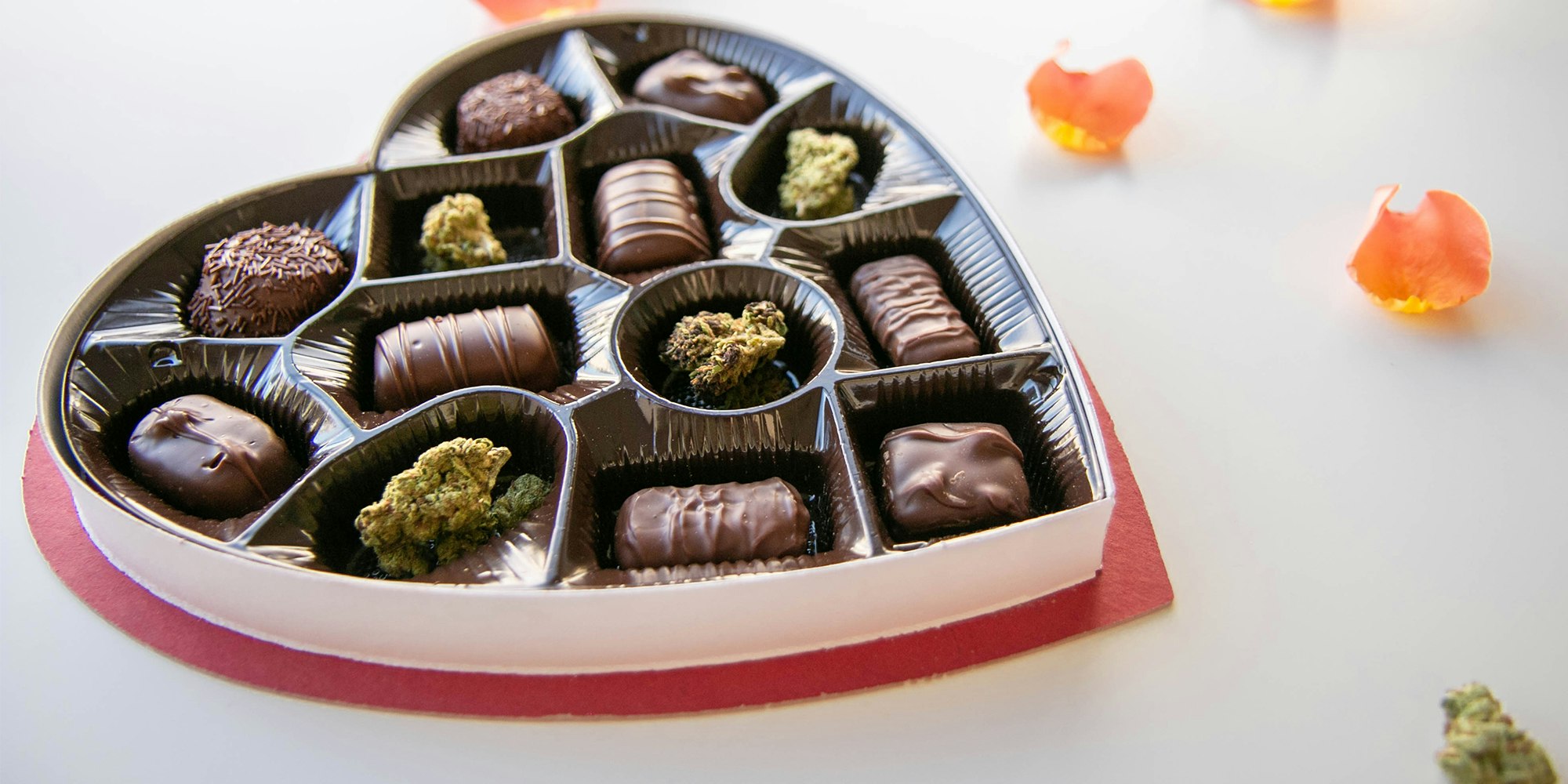 Valentine's Day gift box of chocolates and weed nugs with rose petals scattered around it.