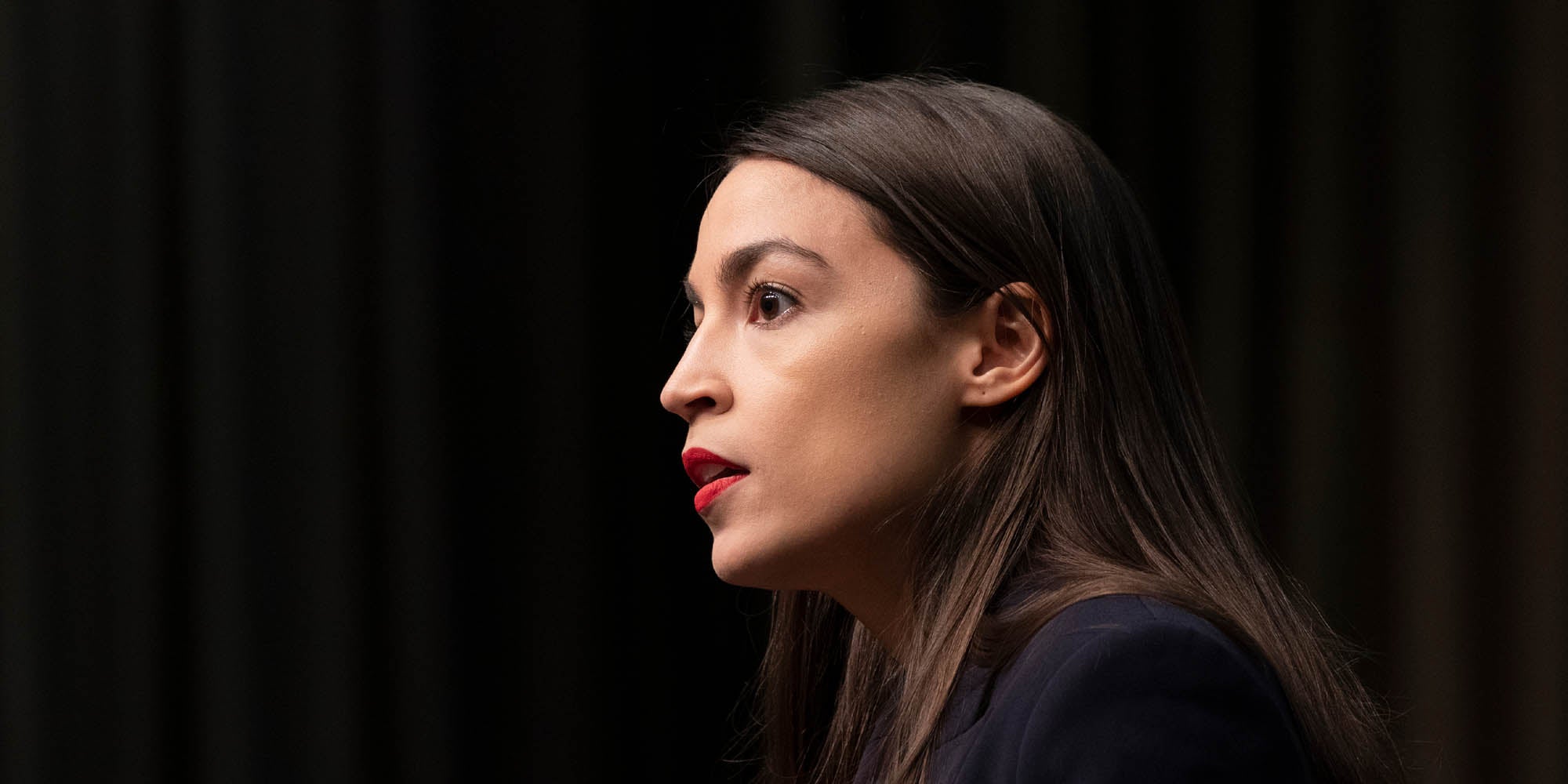 Alexandria Ocasio-Cortez speaking at a podium.