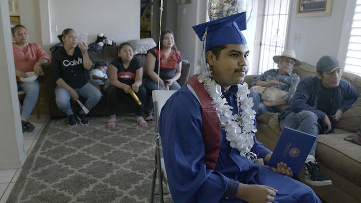 teen wears graduation gown for virtual ceremony as family looks on